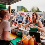 Food Truck Fridays at Tobacco Factory in Bristol. People buying burgers from vendors in the sunny yard.